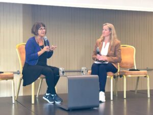 Photo of two women facing toward each other chatting into microphones